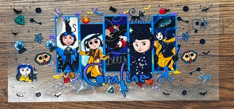 May include: A rectangular clear acrylic sheet featuring a multi-panel illustration of the character Coraline. The design includes the blue-haired protagonist in various outfits, a black cat, keys, buttons, and spiderwebs, with the text Coraline.