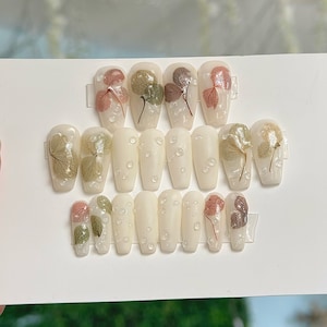 Puede incluir: Conjunto de 14 uñas postizas blancas con detalles de flores secas y un diseño transparente con forma de burbujas. Las uñas son de varios tamaños y formas.