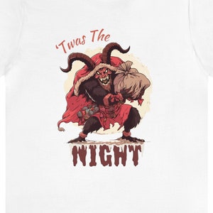 May include: White t-shirt featuring a red and black illustration of a devil holding a bag of gifts. The text "'Twas The NIGHT" is printed below the illustration.