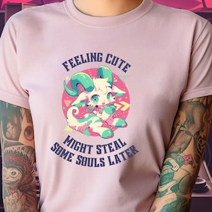 Könnte beinhalten: Pinkes T-Shirt mit einem Comic-Ziegen-Motiv und dem Text "Feeling Cute Might Steal Some Souls Later".