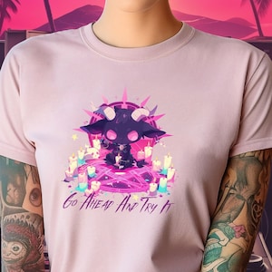 May include: A pink t-shirt with a black and purple cartoon character wearing a crown and surrounded by stars. The text "Go Ahead And Try It" is printed on the shirt.