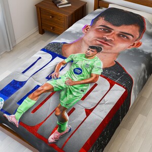May include: A bed blanket featuring a large image of a soccer player in a green uniform, with a secondary, larger image of the same player in the background. The blanket has a red, white, and blue design.
