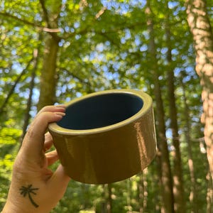 Peut inclure: Un pot en céramique brun avec un glaçage bleu foncé à l'intérieur. Le pot est tenu dans une main avec un tatouage de palmier.