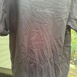 May include: A grey t-shirt featuring the white script text "Collect the Label" on the chest. The shirt has a crew neck and short sleeves. The material looks soft and has some creases.