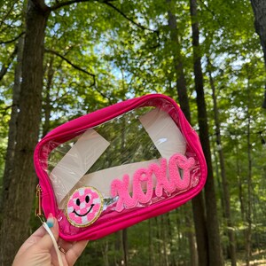 May include: A pink clear plastic bag with a zipper closure. The bag has a pink and white checkered smiley face patch and a pink fuzzy patch that says "XOXO".