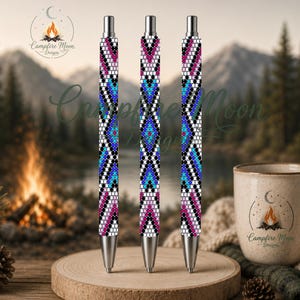 May include: Three retractable pens featuring a repeating geometric pattern in shades of pink, blue, black, and white. Each pen has a silver-toned metal tip and click mechanism at the top, displaying a consistent, intricate, bead-like design.