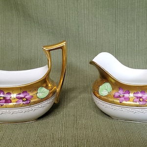 May include: A white porcelain creamer and sugar bowl set with gold accents and purple and green floral designs.