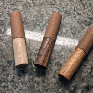 Puede incluir: Tres clavijas de madera con tapas de tela marrón. Las clavijas están hechas de diferentes tipos de madera, incluyendo madera clara, madera oscura y madera rojiza.