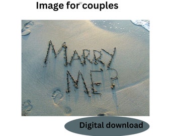 Puede incluir: Las palabras "Marry Me" escritas en la arena de una playa. Las palabras están escritas en una fuente cursiva y están rodeadas de huellas.