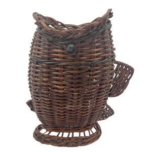 May include: A handcrafted, brown wicker basket shaped like a fish. The basket features woven details, a circular base, and a small, dark button detail. The fish-shaped basket has fins and a tail, and is designed for decorative or storage purposes.