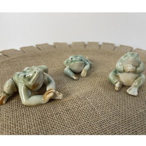 May include: Three ceramic frog figurines in various poses. The frogs are green and white with brown accents.