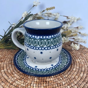 May include: A blue and white ceramic teacup and saucer set with a green and blue floral pattern. The set is sitting on a woven mat.