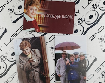 Puede incluir: Dos tarjetas con imágenes del programa de televisión "Se ha escrito un crimen". La primera tarjeta muestra un primer plano de Jessica Fletcher, el personaje principal del programa, con un suéter rojo. La segunda tarjeta muestra a un grupo de personas de pie bajo un paraguas.