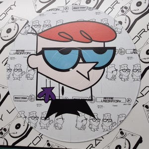 May include: A circular Dexter's Laboratory graphic. The cartoon character Dexter is featured with his signature red hair, blue glasses, and purple tie. The background includes cartoon drawings and text that reads "DEXTER'S LABORATORY".