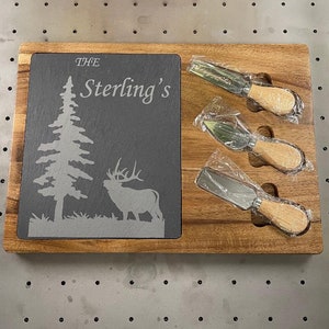 Puede incluir: Una tabla de quesos de madera con una inserción de pizarra. La pizarra está grabada con un árbol, un alce y el nombre "The Sterling's". Se incluyen tres cuchillos para queso con mangos de madera.