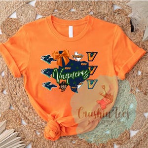 May include: Orange t-shirt with a graphic design featuring a map of Texas in green, the word "Vaqueros" in teal script, and the text "UTRGV". The design includes a bow and other graphics.