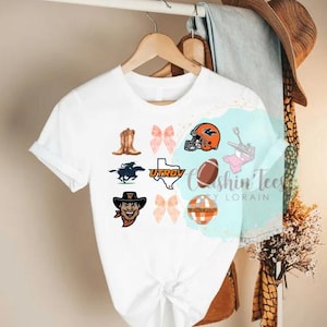 May include: White t-shirt featuring various graphics including a football helmet, cowboy boots, a horse, and the text "UTRGV". The shirt also has a football and a graphic of a cowboy.