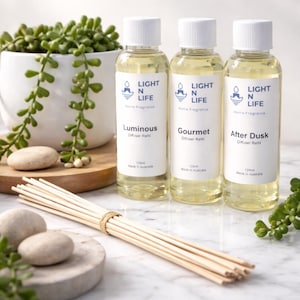 May include: Three glass bottles of home fragrance diffuser refills with white caps and labels. The labels read "Luminous," "Gourmet," and "After Dusk." A bundle of diffuser sticks and a potted plant are also in the image.