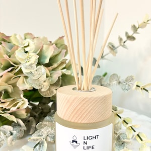 May include: A clear glass bottle with a wooden lid and a label that reads "LIGHT N LIFE Home Fragrance Luminous Fragrance Diffuser 125ml Made in Australia". The bottle is filled with a clear liquid and has wooden sticks sticking out of the top.