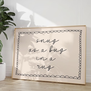 Peut inclure: Une affiche beige avec une bordure noire et une citation manuscrite noire qui dit "snug as a bug in a rug".