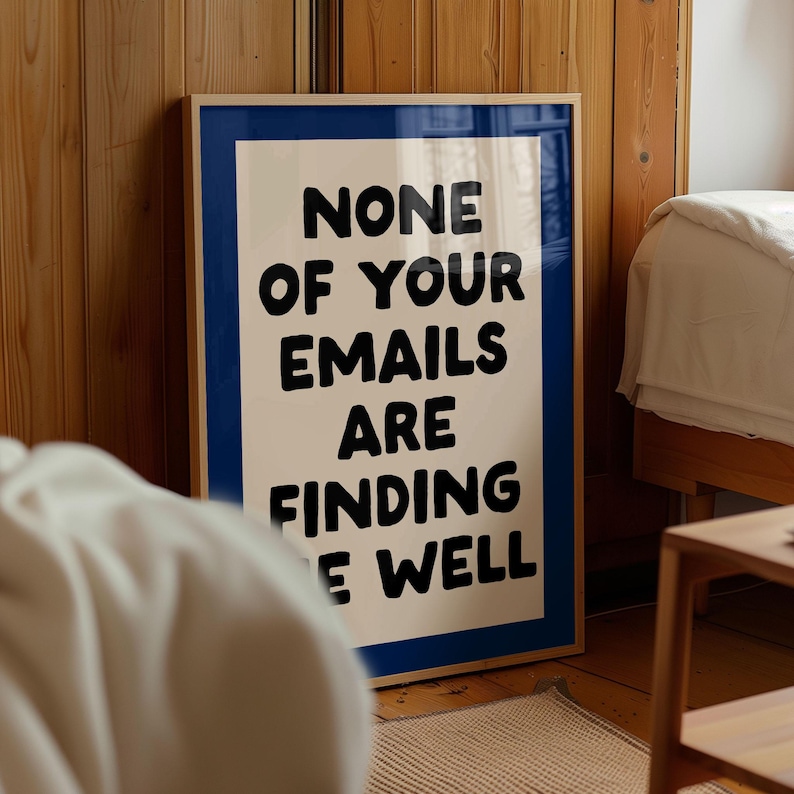 May include: A framed poster with the text "NONE OF YOUR EMAILS ARE FINDING E WELL" in bold black letters. The poster has a white background with a blue border and a wooden frame. The poster is leaning against a wooden wall.