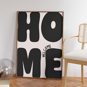 Könnte beinhalten: Schwarz-weiß Druck mit dem Wort "HOME" in großen, stilisierten Buchstaben. Das Wort "WELCOME" ist in kleineren Buchstaben innerhalb des Buchstabens "M" geschrieben.