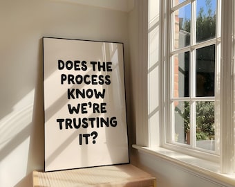 May include: A rectangular framed wall art piece featuring a cream-colored background with bold, black, rounded sans-serif text that reads: DOES THE PROCESS KNOW WE'RE TRUSTING IT? The print is displayed in a thin black frame with a clean, simple design.