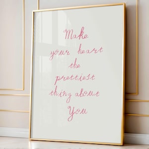 Könnte beinhalten: Ein gerahmter Kunstdruck mit einem goldenen Rahmen. Der Druck zeigt den handgeschriebenen Text "Make your heart the prettiest thing about you" in rosa Schrift auf weißem Hintergrund. Das Kunstwerk wird vor einer neutralen Wand ausgestellt.
