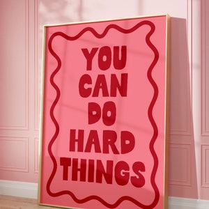 Puede incluir: Un póster motivacional rosa con marco dorado. El póster presenta un borde ondulado y el texto "YOU CAN DO HARD THINGS" en rojo.