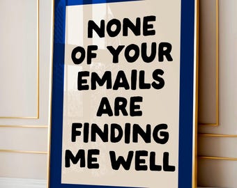 Pode incluir: Uma impressão de arte emoldurada com uma moldura dourada e uma passe-partout azul marinho. A obra de arte apresenta o texto "NONE OF YOUR EMAILS ARE FINDING ME WELL" em letras pretas em negrito sobre um fundo creme. A impressão é exibida contra uma parede neutra.