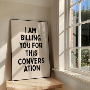 Può includere: Un quadro rettangolare incorniciato con sfondo bianco e testo nero in grassetto che recita I AM BILLING YOU FOR THIS CONVERSATION. La stampa è racchiusa in una sottile cornice nera ed è posizionata in verticale su una superficie intrecciata.