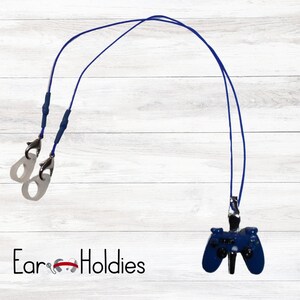 May include: A blue lanyard featuring a video game controller charm. The lanyard has two clear earbud holders with silver clasps. The controller charm is dark blue with black details. The text "Ear Holdies" is at the bottom.