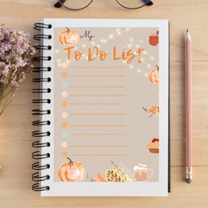 Op de afbeelding: Een bruin notitieboekje met een to-do-lijst met een herfstthema. De omslag heeft pompoenen, bladeren en een kopje koffie. De tekst "My To Do List" staat in wit op de omslag.