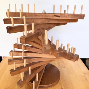 May include: A multi-tiered wooden display stand featuring a central vertical axis with rotating horizontal arms. Each arm is constructed from stained brown wood and is fitted with multiple light-colored wooden pegs for hanging items.