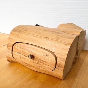 May include: A wooden box carved from a tree trunk with a drawer that has a round knob. The box is light brown and has a natural wood finish.