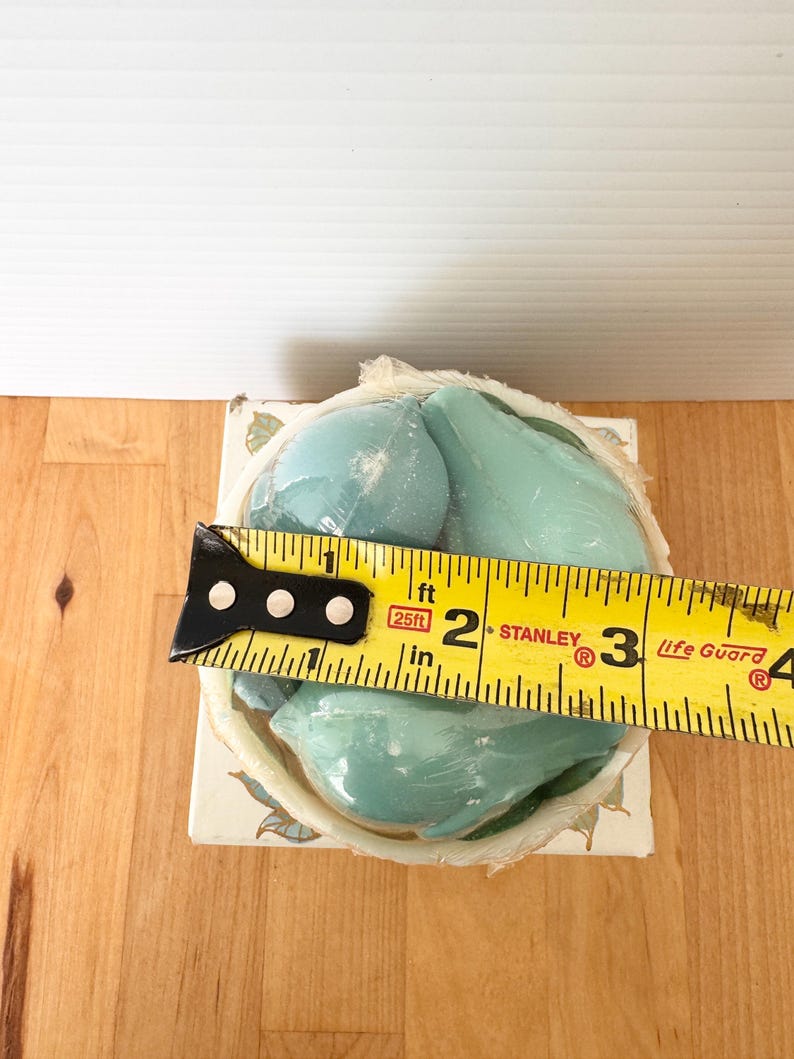 Puede incluir: Un juego de jabones en forma de pera de color azul claro, envuelto en pl&aacute;stico transparente, se encuentra en una caja decorativa. La caja est&aacute; decorada con motivos florales. Una cinta m&eacute;trica amarilla muestra que el juego de jabones mide aproximadamente 7,6 cm de ancho.