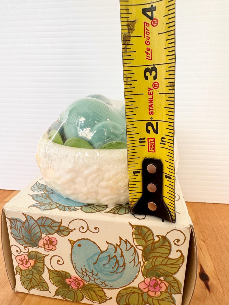 Puede incluir: Figura de p&aacute;jaro de cer&aacute;mica en un nido, empaquetada en una caja decorativa. El nido es blanco con una superficie texturizada, y el p&aacute;jaro est&aacute; envuelto en pl&aacute;stico. La caja presenta una ilustraci&oacute;n de p&aacute;jaro azul con dise&ntilde;os florales y de hojas. La altura es de aproximadamente 7,6 cm.