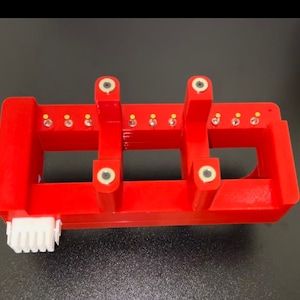 May include: Red plastic component with multiple gold-colored pins and four black circular connectors. The component has a white plastic connector on the side.