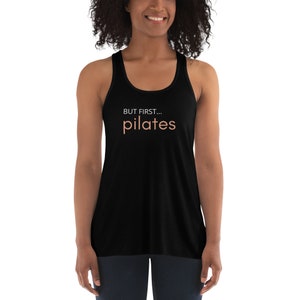 May include: Black racerback tank top with the text "BUT FIRST... pilates" in white and peach.