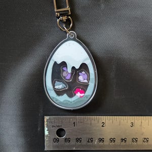 Puede incluir: Llavero acr&iacute;lico transparente en forma de huevo con cierre plateado. El llavero presenta un dise&ntilde;o de varios animales de dibujos animados en un huevo. El llavero mide aproximadamente 5 cm de largo.