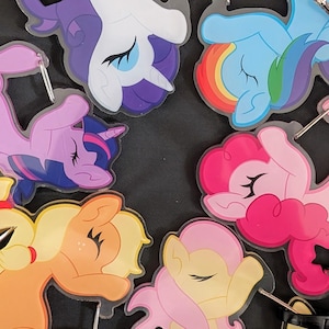 May include: A collection of colorful cartoon pony-shaped keychains. The keychains feature various ponies in shades of purple, pink, yellow, blue, and orange. Each keychain has a silver-colored metal ring attached for easy use.