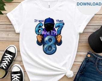 May include: White t-shirt featuring a cartoon graphic with the text "It was then 67 Now I'm 8". The graphic shows a person wearing a blue cap and holding the numbers 6, 7, and 8. The design is in shades of blue.