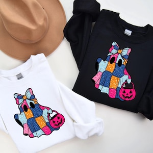 Puede incluir: Dos sudaderas de manga larga, una blanca y otra negra, cada una con un diseño de fantasma colorido. El fantasma está adornado con un patrón de patchwork, un lazo y una cesta de calabaza rosa, ideal para Halloween.