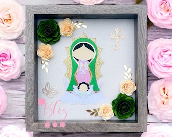 May include: A framed picture with a paper cutout of the Virgin Mary and baby Jesus. The frame is made of wood and has a gray finish. The picture is surrounded by paper flowers in shades of pink, green, and peach.