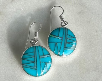 May include: A pair of silver dangle earrings with turquoise and opal inlay. The earrings feature a geometric design with a blue and white color scheme.