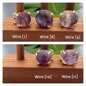 May include: Five gold rings with purple amethyst stones. The rings are displayed on a wooden stand. Wire [7], Wire [8], Wire [9], Wire [10], Wire [11].