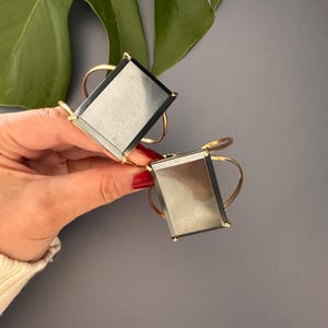 May include: Two gold-toned bracelets with rectangular black stones. The stones have a reflective surface.