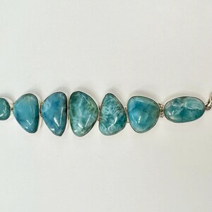 May include: A silver bracelet with a row of six light blue and green gemstone beads. The bracelet has a toggle clasp on one end and a ring clasp on the other.