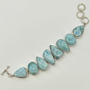 May include: A silver bracelet with a row of light blue teardrop-shaped gemstones. The bracelet has a toggle clasp.