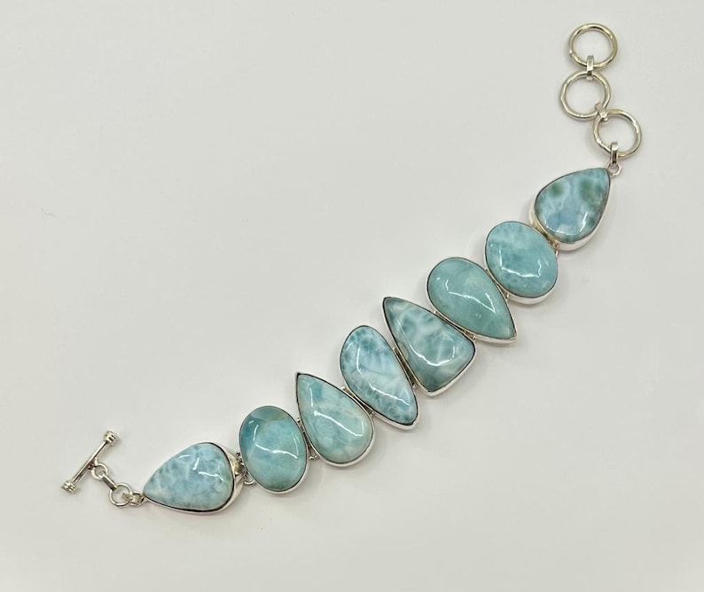 May include: A silver bracelet with a row of light blue teardrop-shaped gemstones. The bracelet has a toggle clasp.